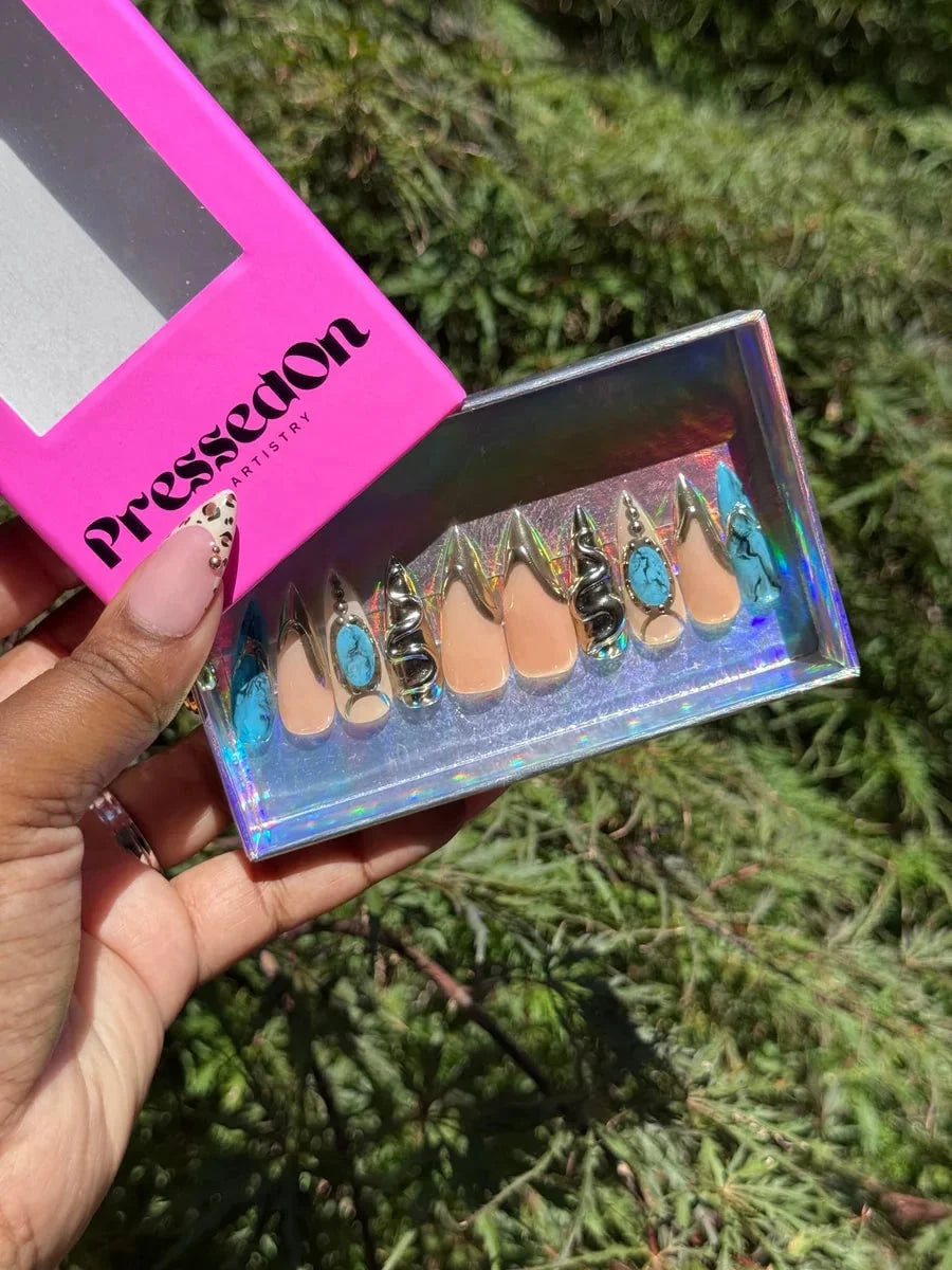 Medium press-on nails with a nude base and gold accents. Some nails have a blue 'croc' texture, while others have 3D snake embellishments or turquoise stone decorations. Includes both almond and stiletto shapes.
