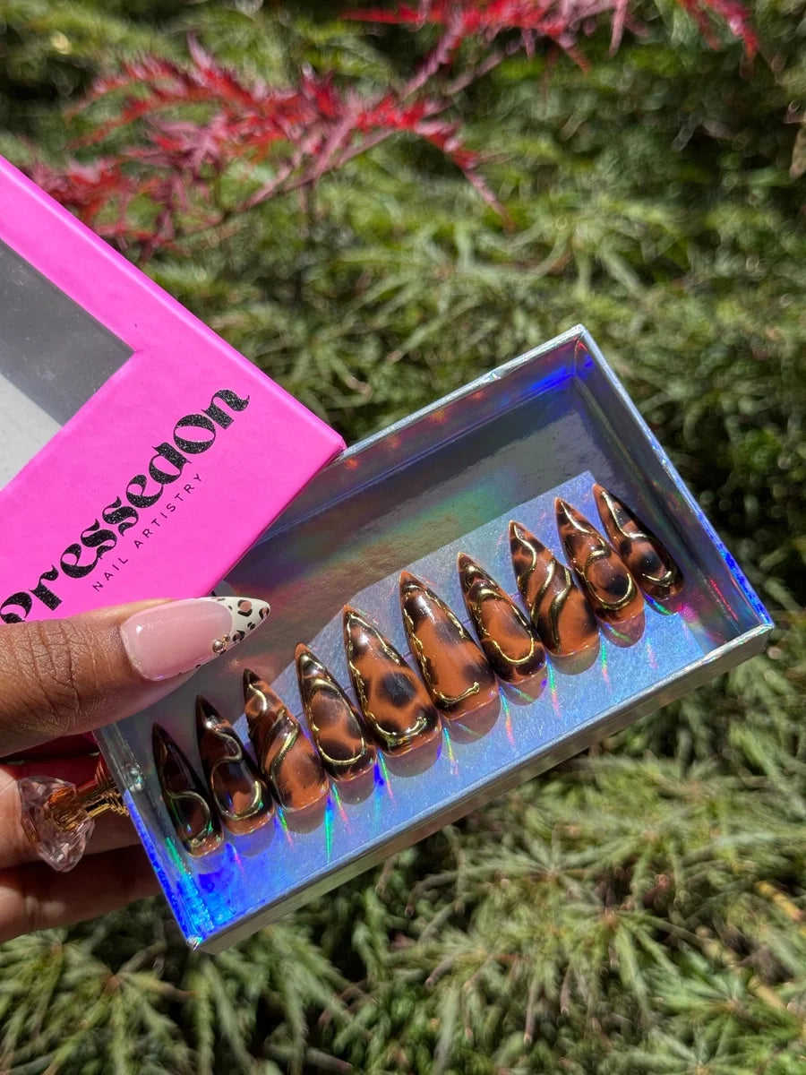 Medium stiletto press-on nails with a brown cheetah print design and 3D gold accents. The nails feature a glossy finish.