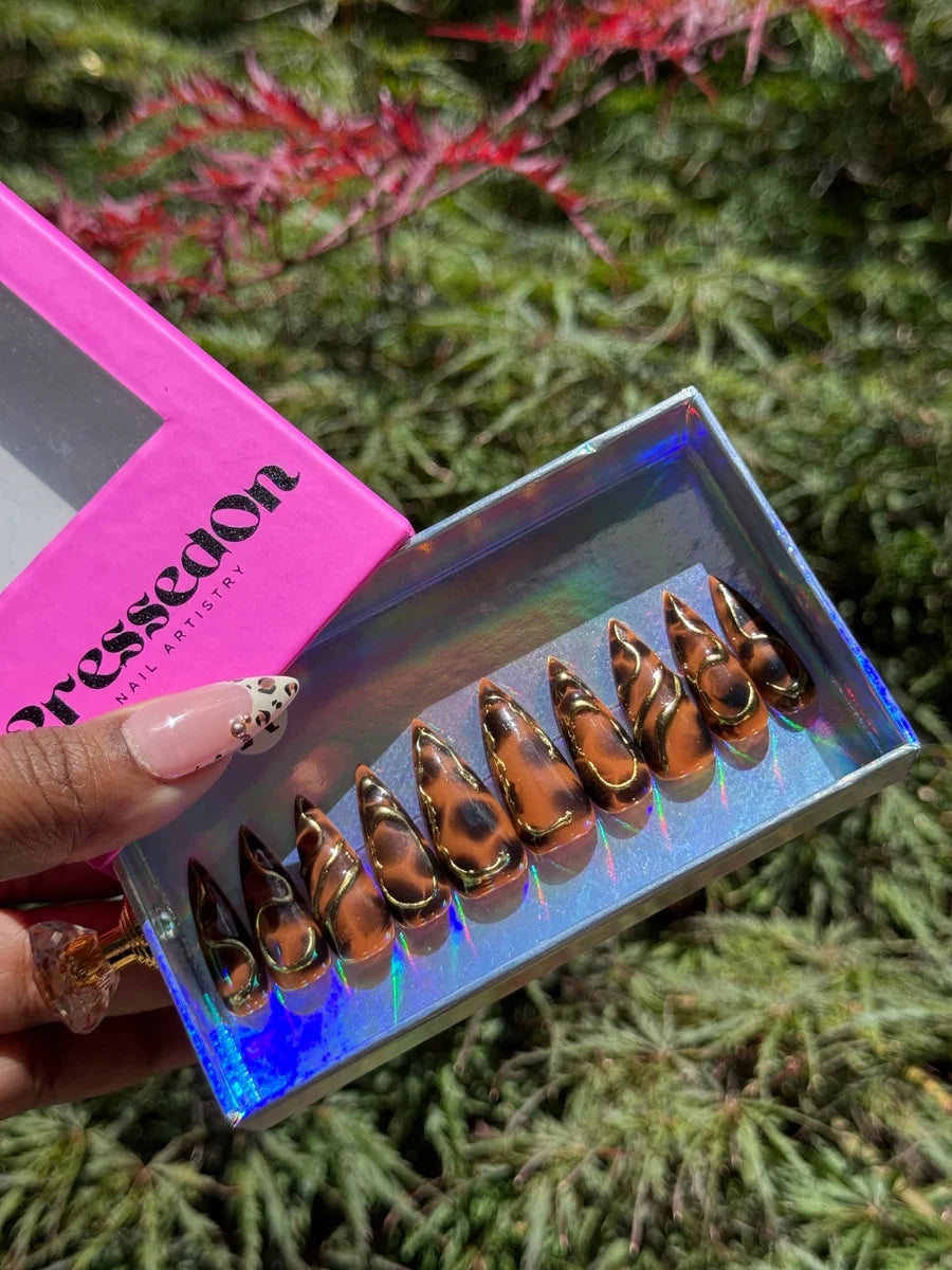 Medium stiletto press-on nails featuring a brown cheetah print with 3D gold accents. The nails have a glossy finish.