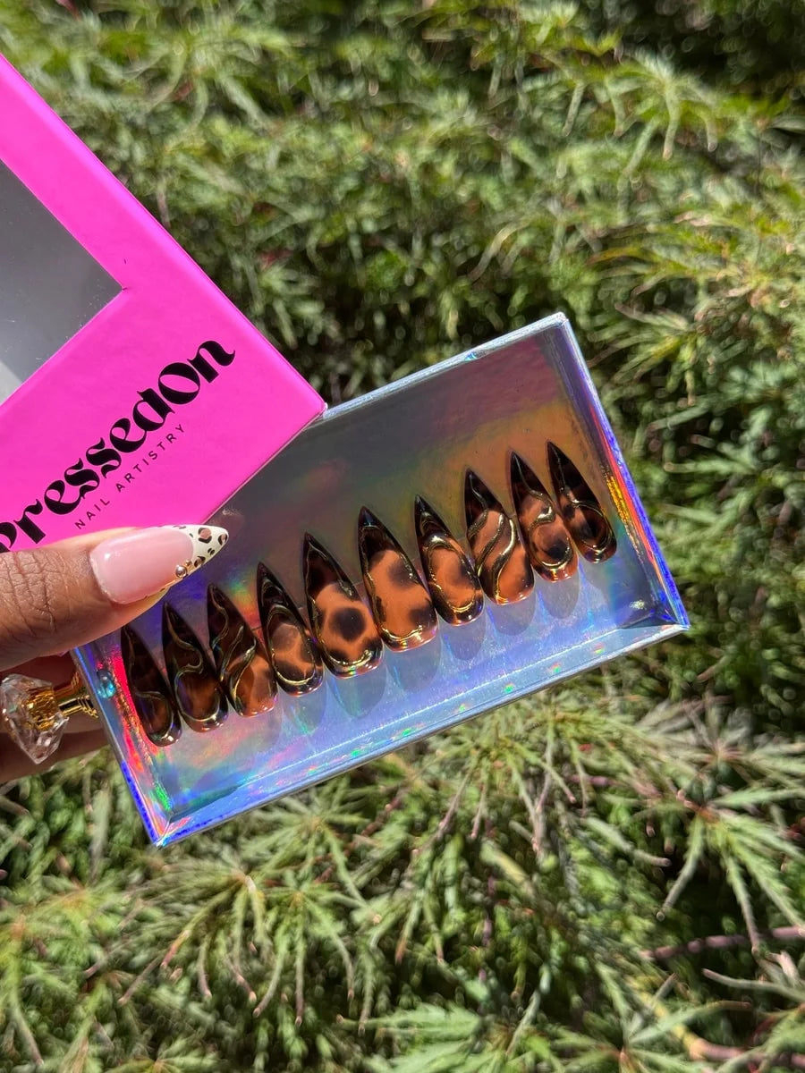 Medium stiletto acrylic press-on nails display a 3D brown cheetah print with metallic gold accents. The design features a glossy finish.