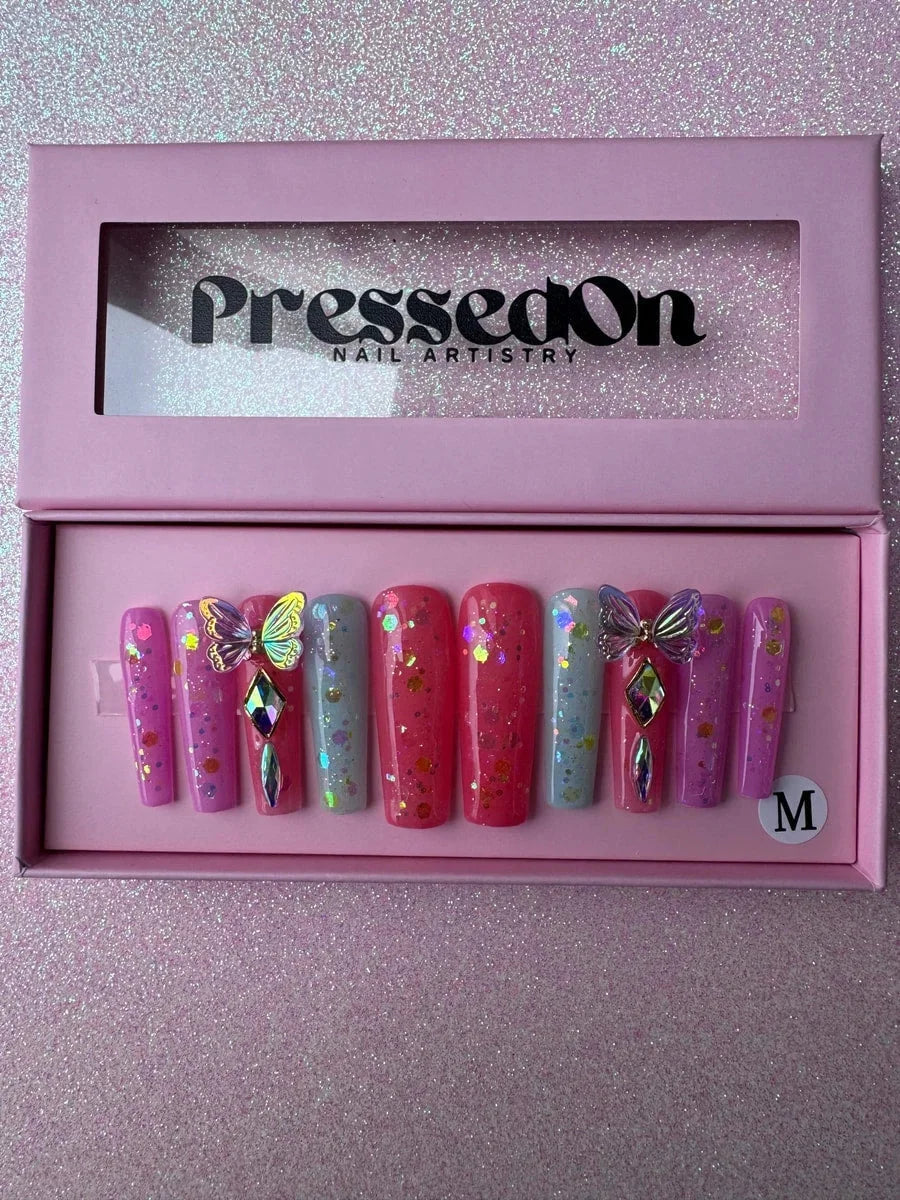 Long coffin press-on nails in shades of pink and light blue with glitter. Two nails are decorated with 3D butterflies and rhinestone gems.