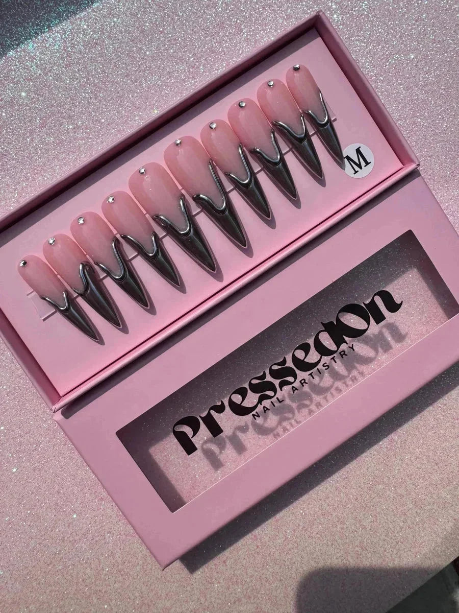 Long pink stiletto press-on nails with chrome accents. Each nail also features a small rhinestone near the base.