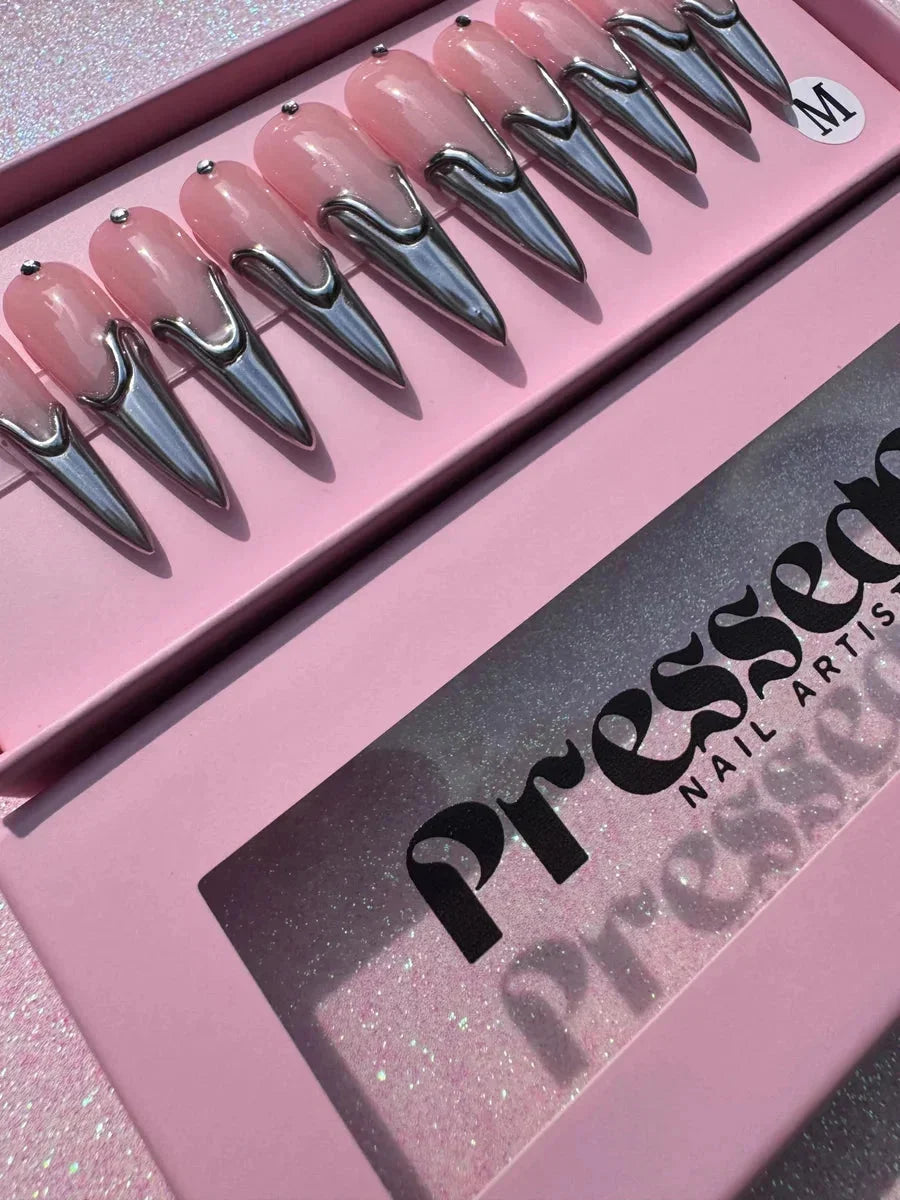 Long pink stiletto press-on nails feature a silver chrome design. The nails have a glossy pink base with a metallic silver accent near the tips.