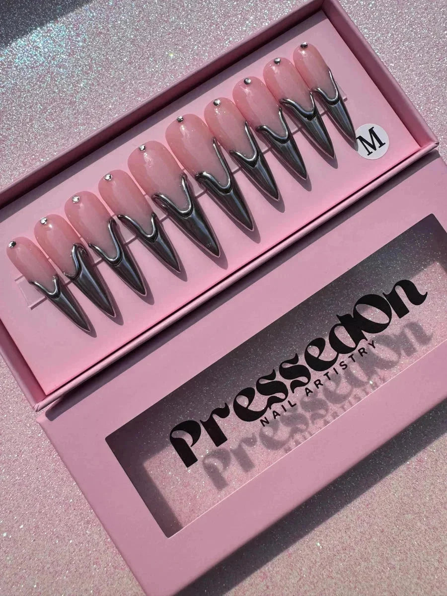 Long pink stiletto press-on nails feature chrome accents and rhinestone embellishments.