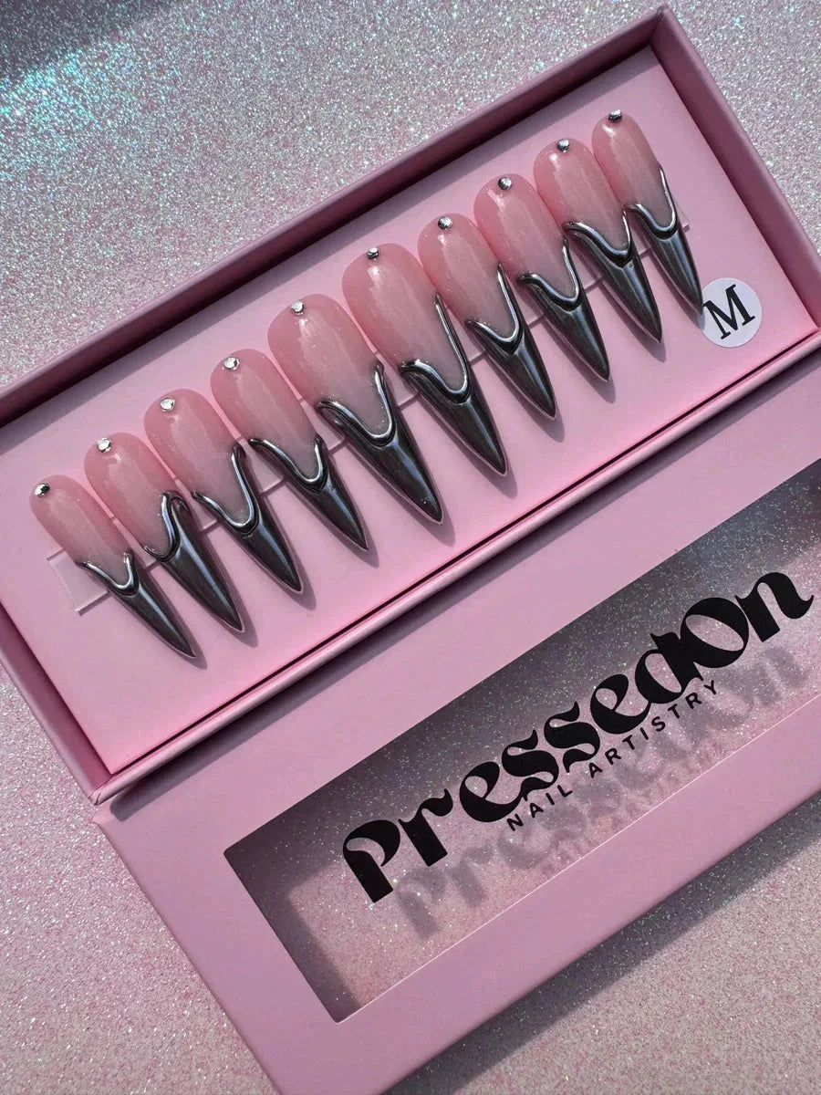 Long pink stiletto press-on nails featuring chrome accents and tiny rhinestones. The nails have a pink base color with a sharp, reflective chrome tip design.