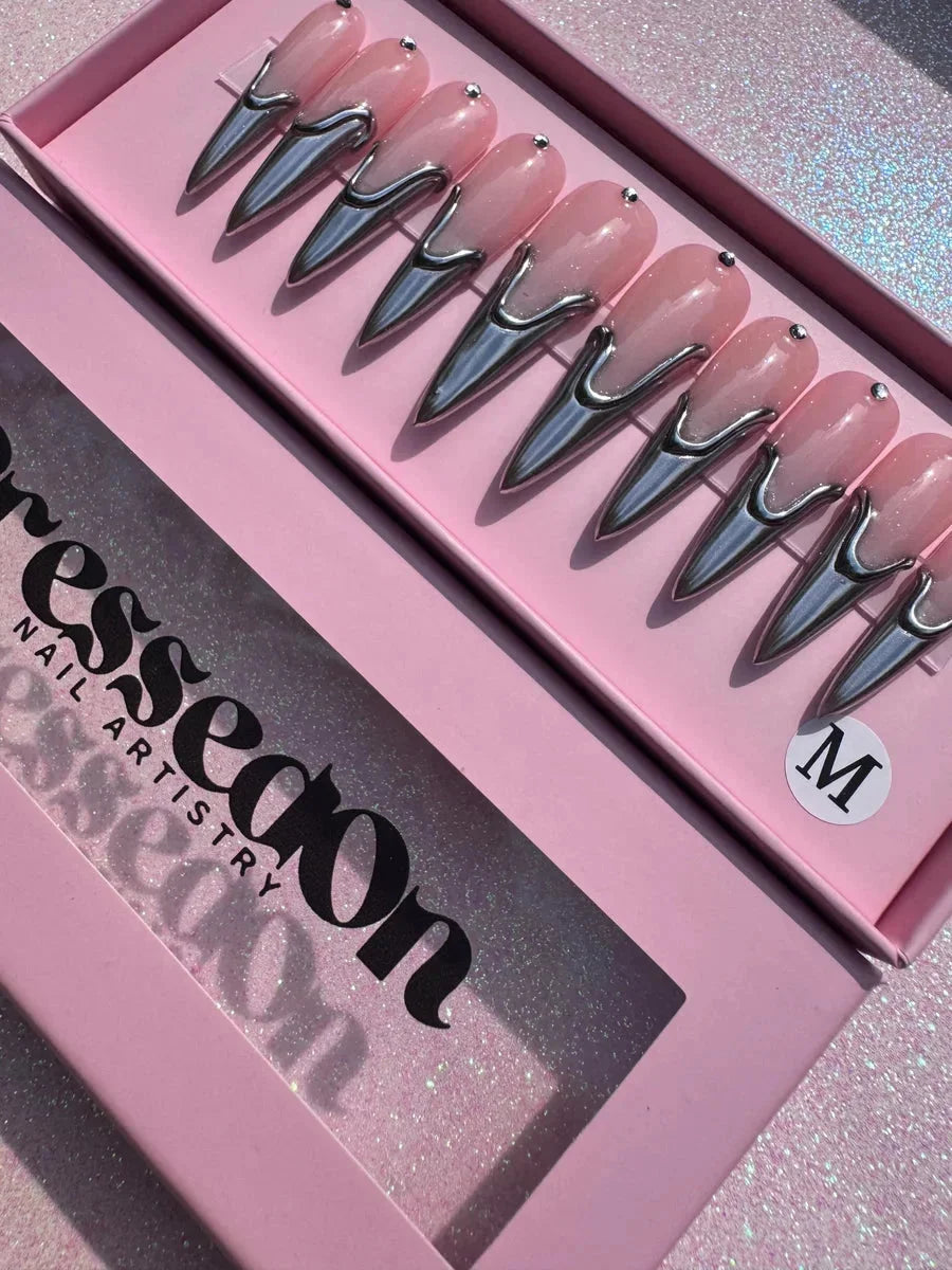 Long, pink stiletto press-on nails with a chrome accent near the base and a small rhinestone near the cuticle. The nails have a glossy finish.