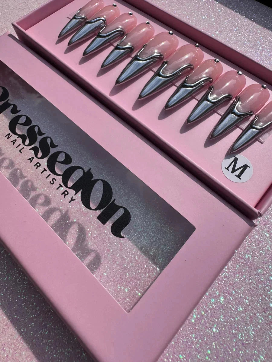 Long pink stiletto press-on nails featuring a metallic silver chrome 3D design accent. The nails have a pointed shape.