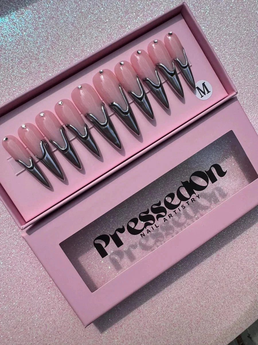 Long pink stiletto press-on nails with a unique silver chrome design at the tips and small rhinestone decorations near the base.