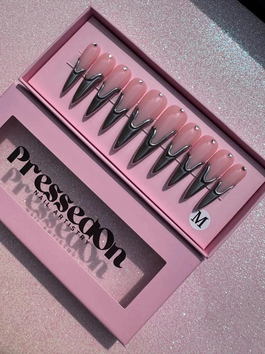 Long pink stiletto press-on nails with a chrome metallic v-shaped accent at the base and a small rhinestone detail near the cuticle.