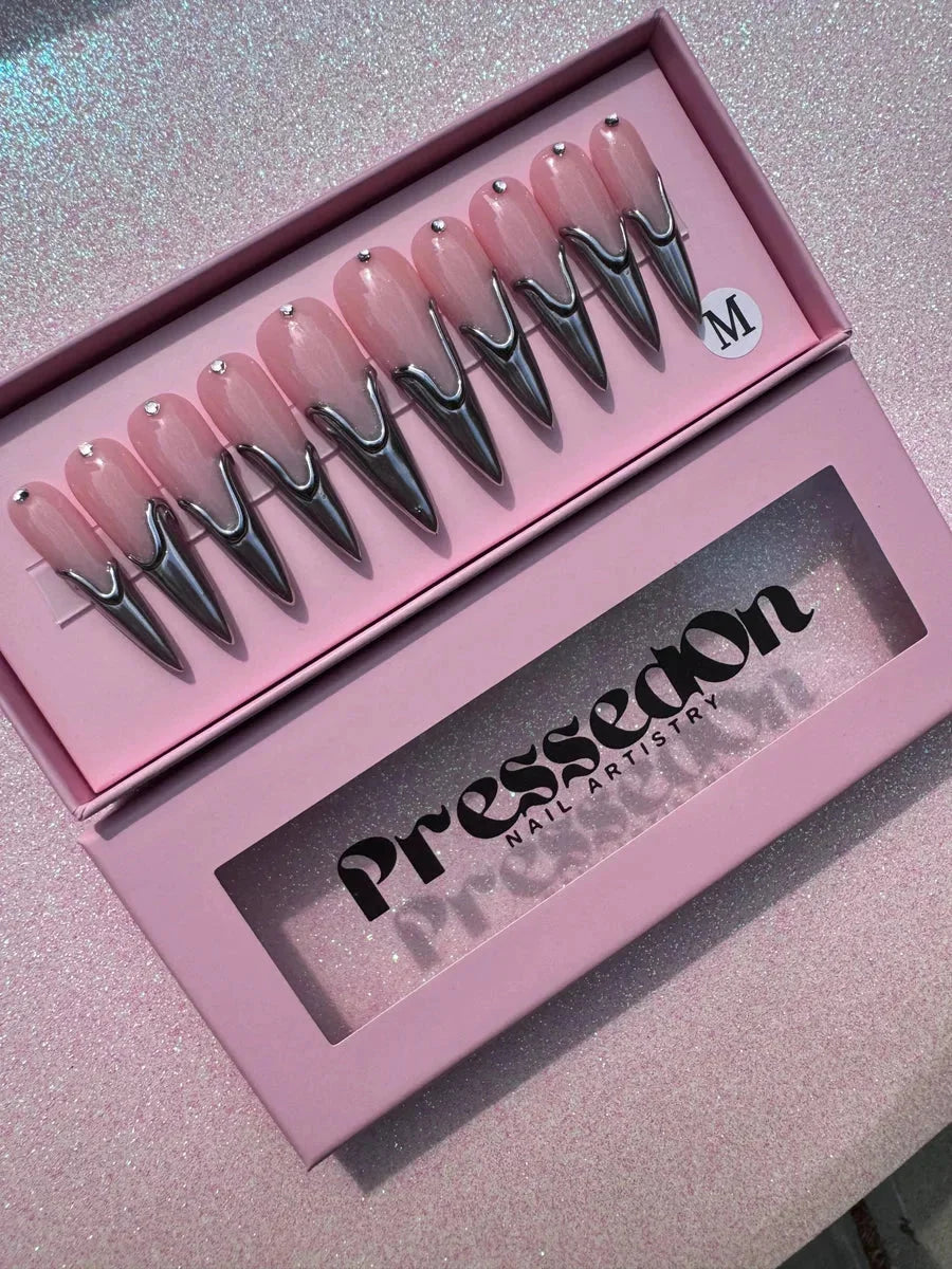 Long pink stiletto press-on nails feature chrome metallic tips and a rhinestone accent at the base.