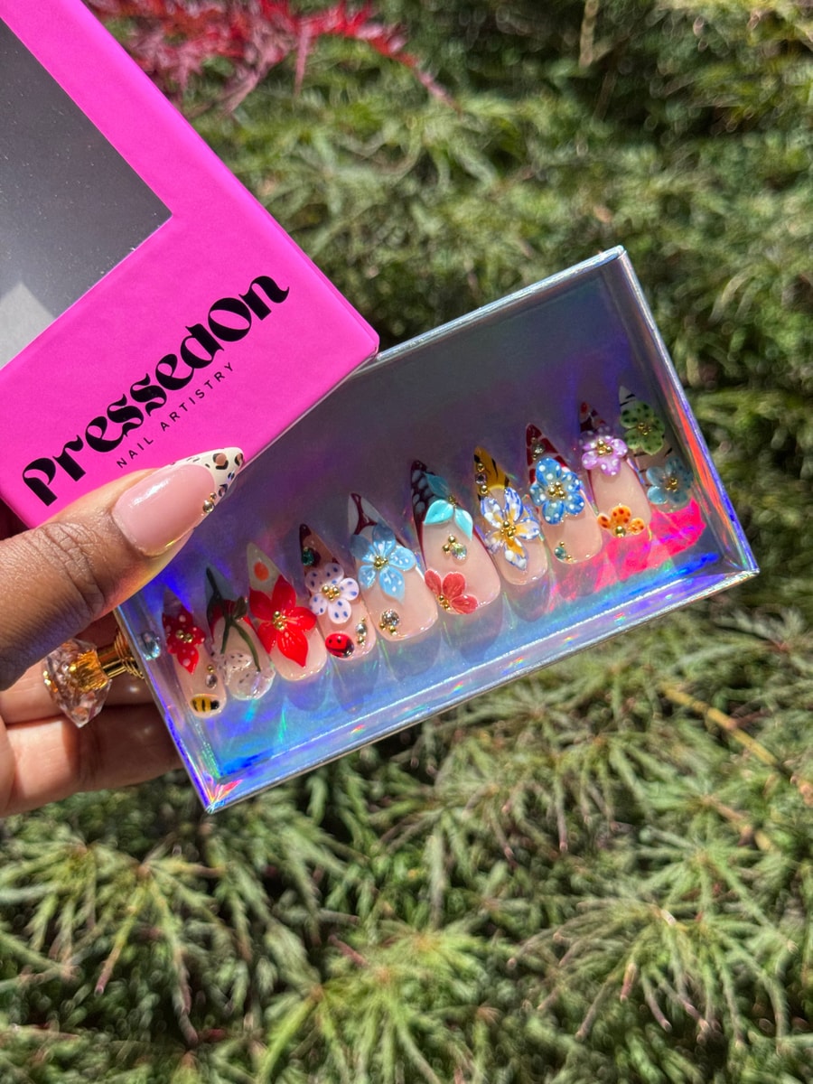 Medium-length press-on nails featuring a nude base with detailed 3D floral designs, including various flower colors, ladybug, and bee embellishments.