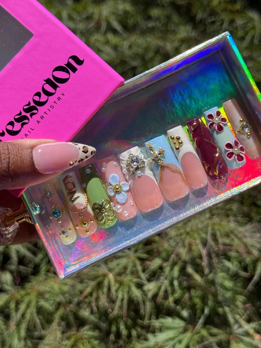 A set of medium press-on nails featuring a mix of French tips, floral designs, and a leopard print accent nail. Some nails have 3D embellishments and gold details.