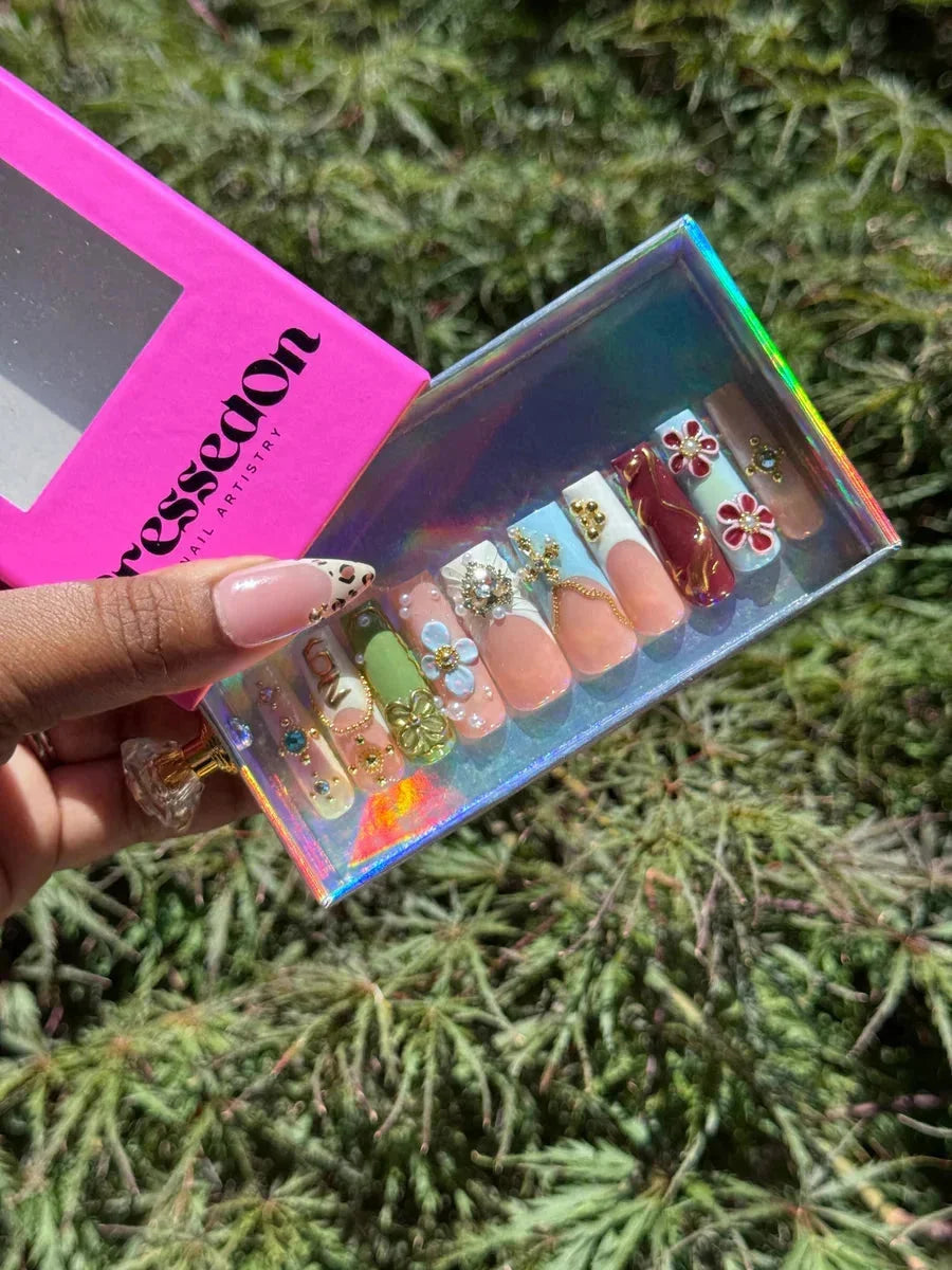 Assorted press-on nails with 3D floral, leopard, and French tip designs. Features include gold accents, pearl embellishments, and a mix of colors.