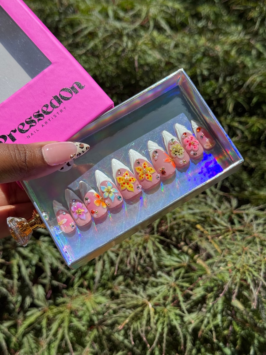 Short stiletto press-on nails with a French tip and a pink base, decorated with 3D flowers, rhinestones, and pearl beads.