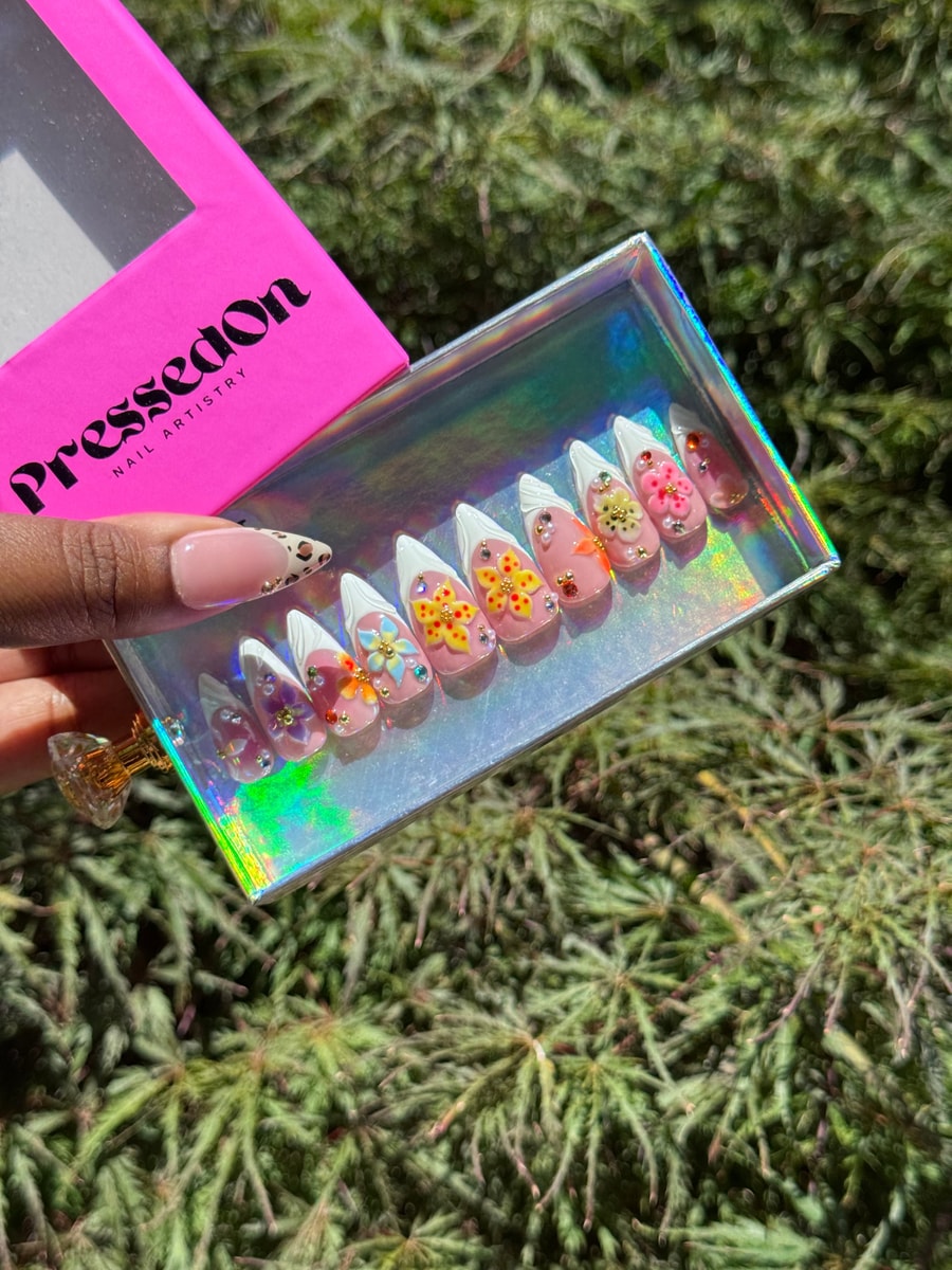 Short press-on nails with pink base, white French tips, and 3D flower accents. One nail has a cheetah print design.