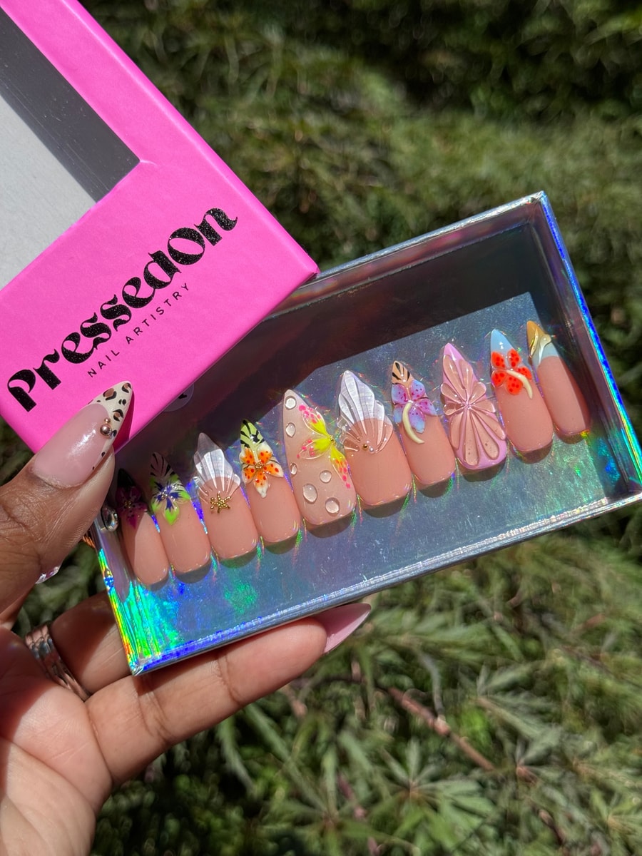 A set of medium-length nude press-on nails decorated with colorful 3D flower and butterfly accents and water droplet details.