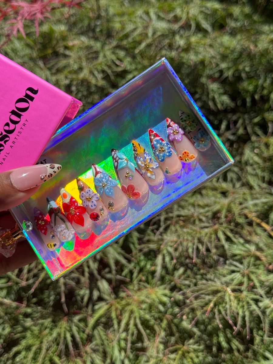 Medium-length press-on nails with intricate 3D floral designs. Each nail features a different vibrant flower with embellishments.