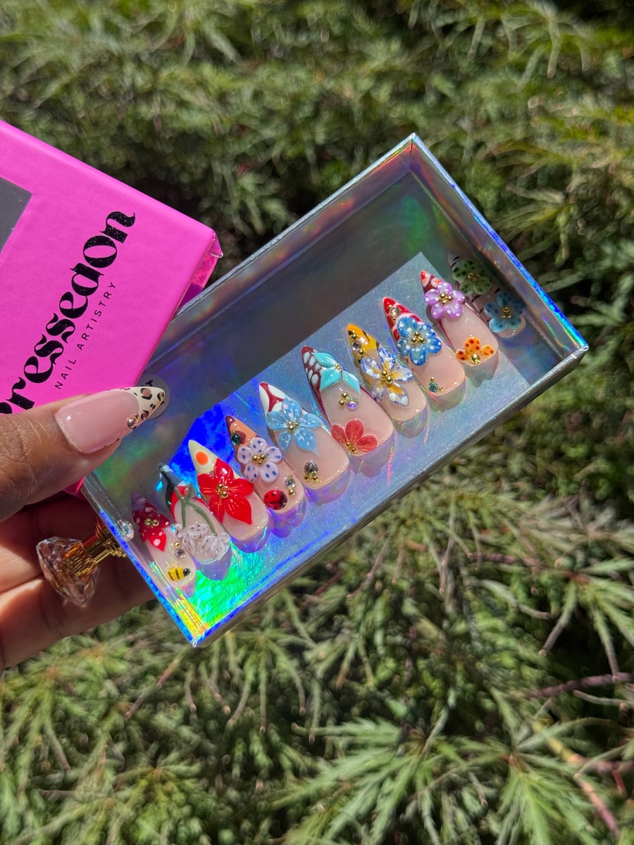 Medium press-on nails feature a nude base with colorful 3D floral embellishments and rhinestone accents.