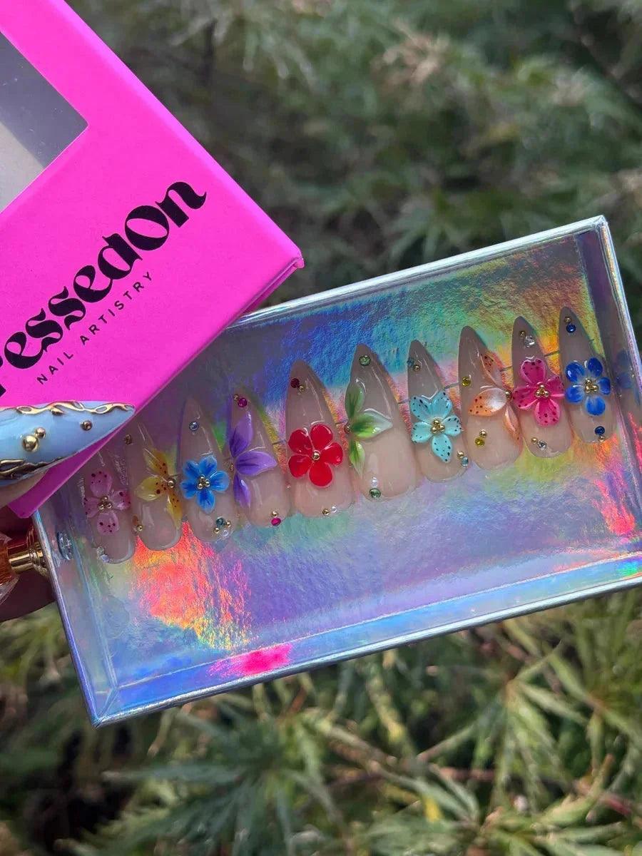 Nude short stiletto press-on nails decorated with colorful 3D hibiscus flowers and small rhinestones.