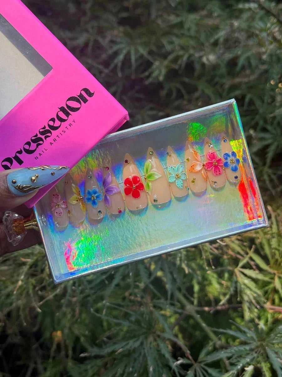 Short stiletto nude press-on nails with 3D hibiscus flower designs in various colors and small rhinestone accents.