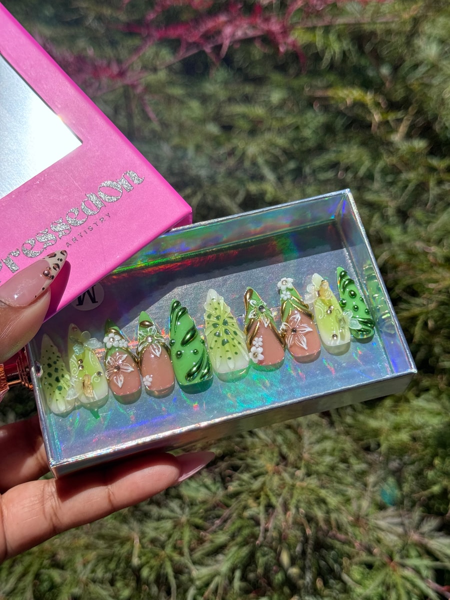 A set of medium-length press-on nails with a 3D kiwi-inspired design in various shades of green, featuring flower accents and intricate detailing on each nail.