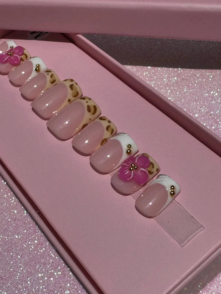 Super short press-on nails with French tips and cheetah print. Some have pink 3D flowers and gold beads on a sheer pink base.