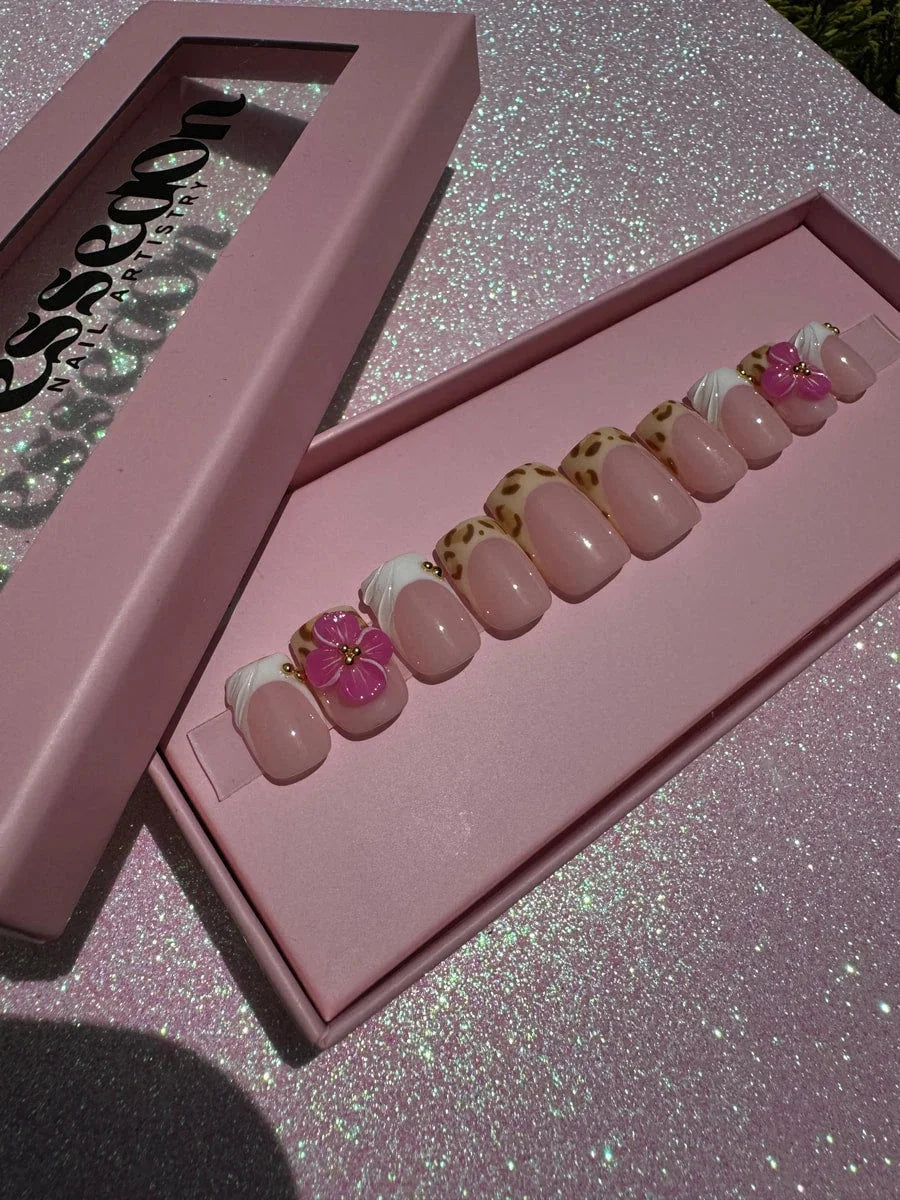 Super short press-on nails with a cheetah print, French tips, and 3D pink hibiscus flower embellishments. Some nails have a sheer pink base and gold bead accents.