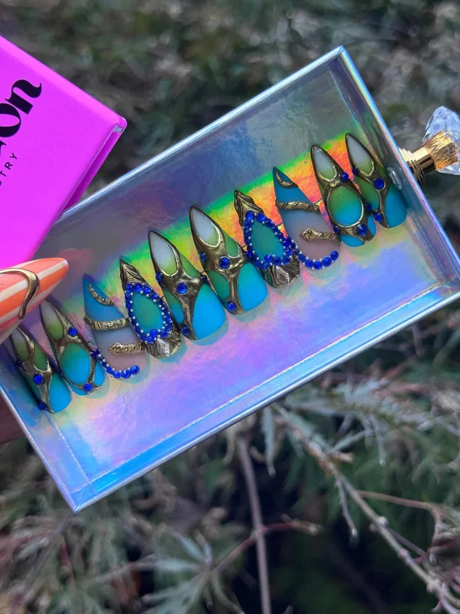 Aqua pointed press-on nails with blue gemstones and a gold snake design. The nails feature a blend of aqua and seafoam green with gold detailing.