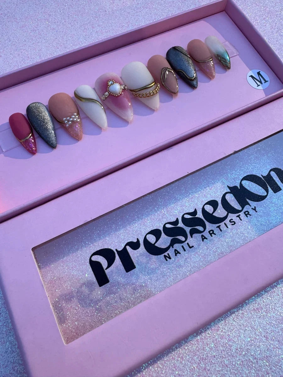 Medium almond-shaped press-on nails feature pink, silver and blue glitter, and nude shades with gold accents, gold chains, and heart embellishments.
