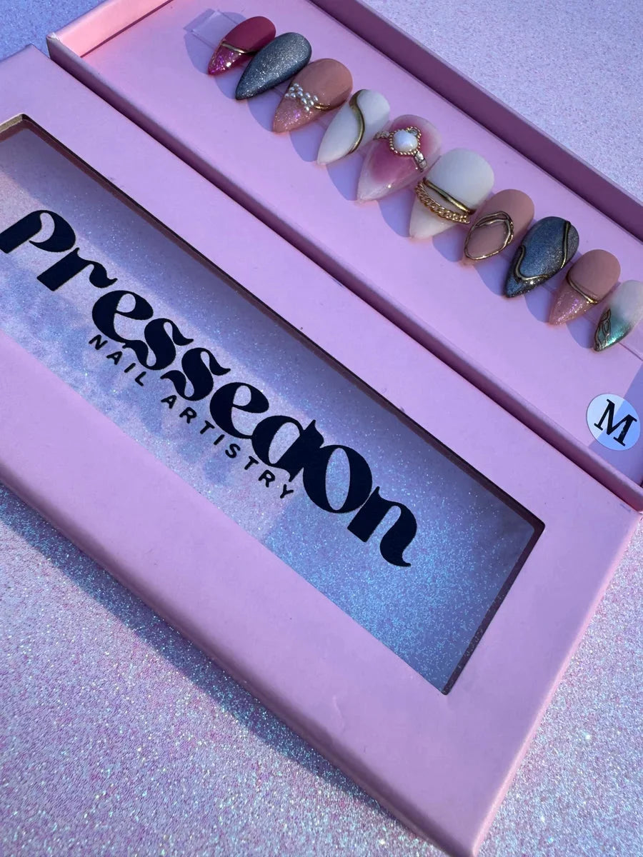 Almond-shaped medium press-on nails with unique designs featuring glitter, rhinestones, gold chains and accents in shades of pink, grey, white, and nude.