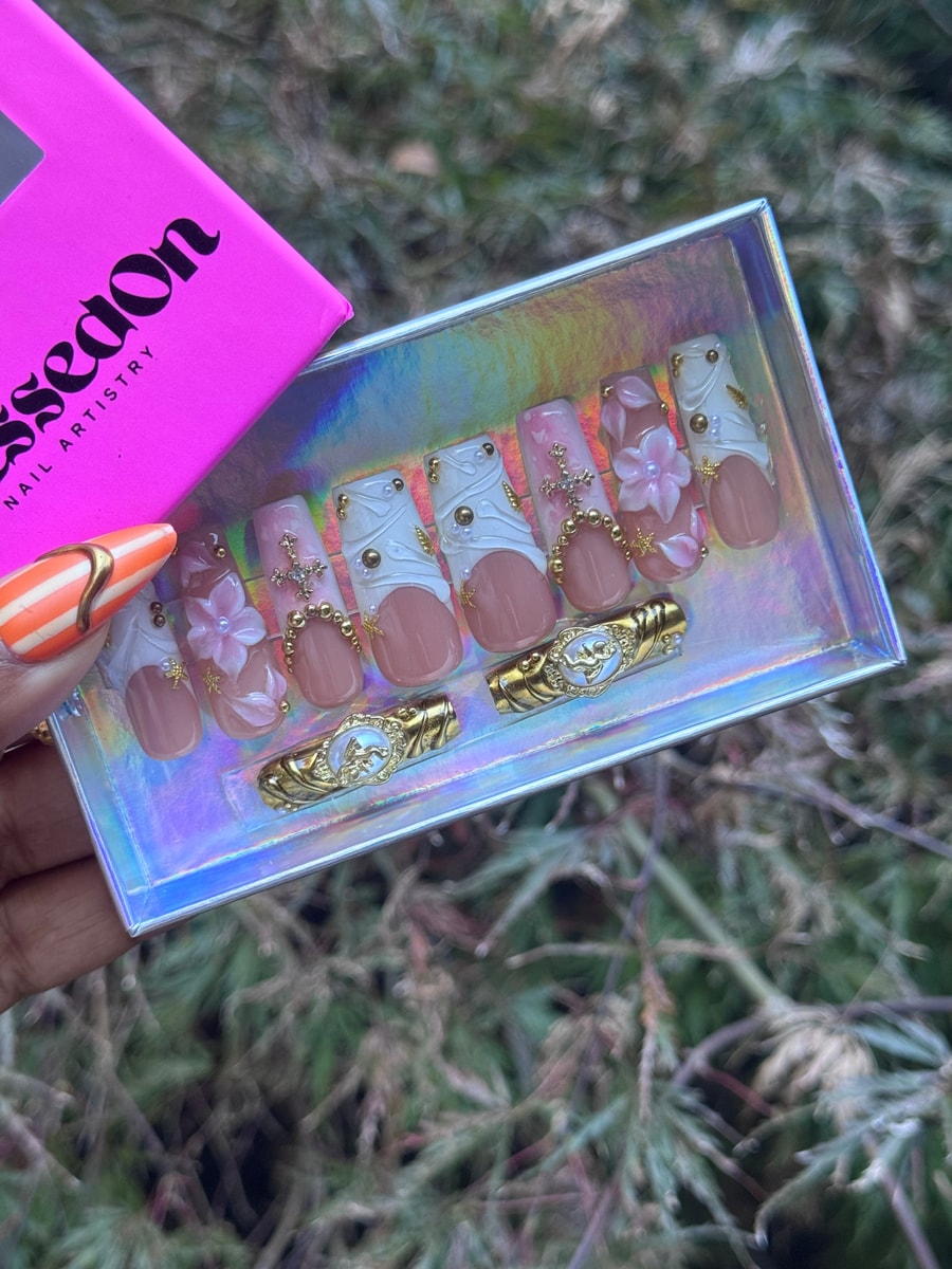 Medium press-on nails showcase a bloom style design with pink, white, gold, cross, and pearl accents.