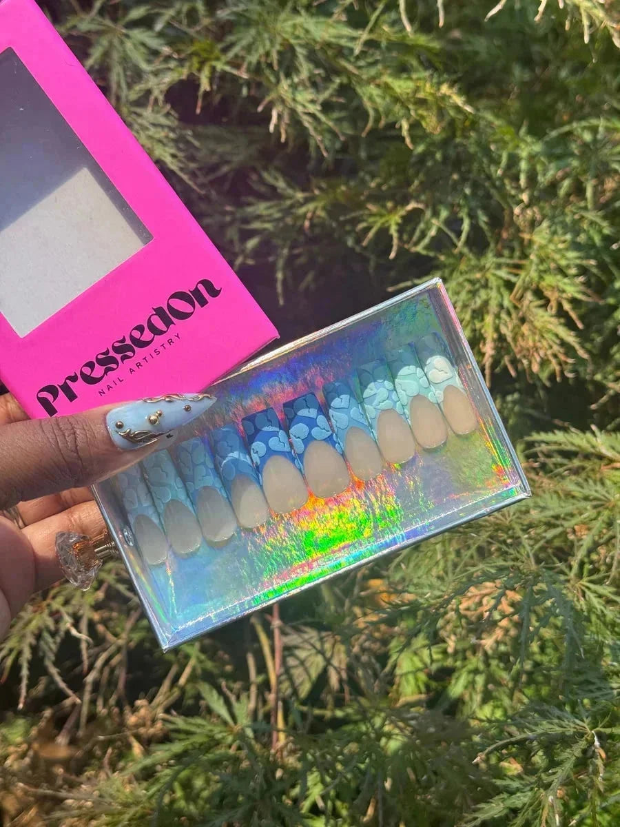 These are short, rounded press-on nails with a nude base and blue broken heart designs on the French tips. The French tips have a white outline.