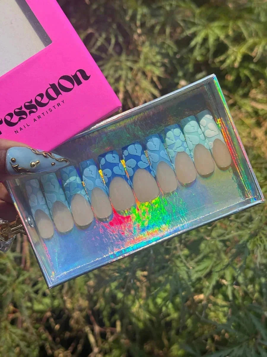 Short press-on nails featuring a nude base and a French tip design with broken heart patterns in varying shades of blue.