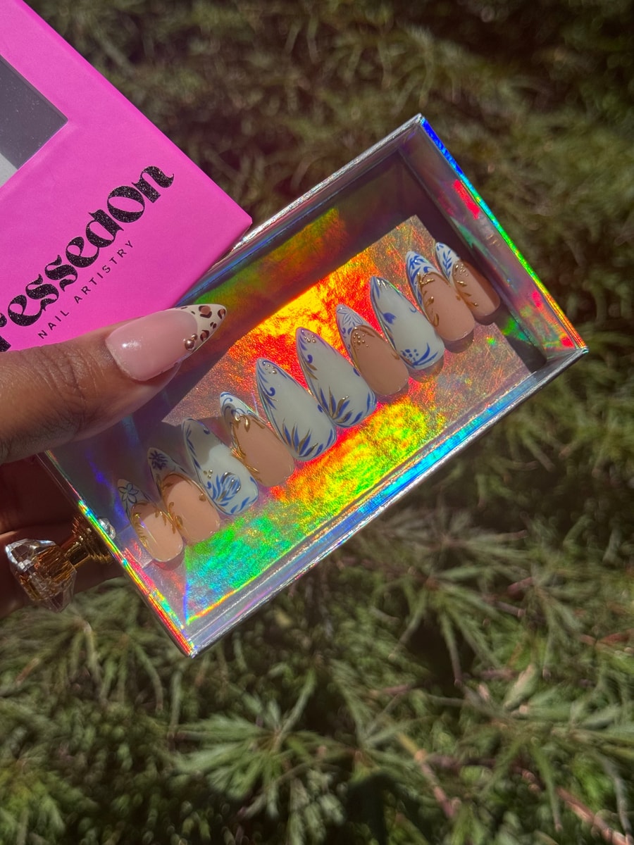 Short press-on nails feature a blue and white floral design with nude accent nails detailed with delicate gold.