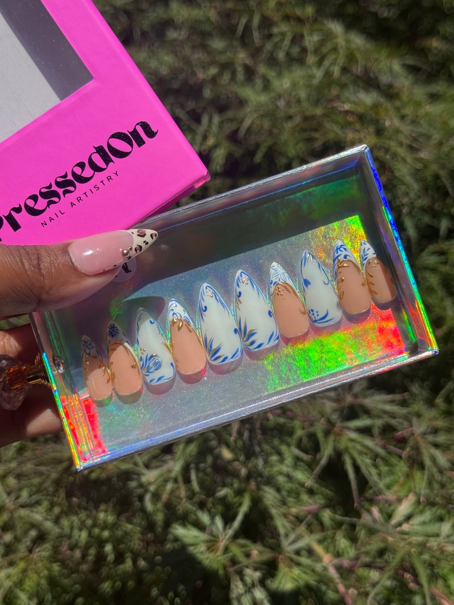 This set of short stiletto press-on nails features a combination of blue, white, and nude colors with delicate floral designs and gold accents.