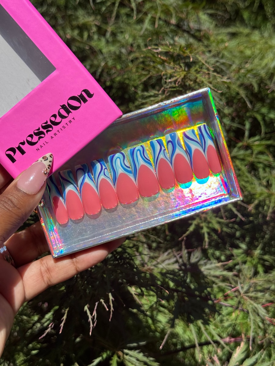 Set of medium length press-on nails with a coral pink base and wavy blue and white accents.