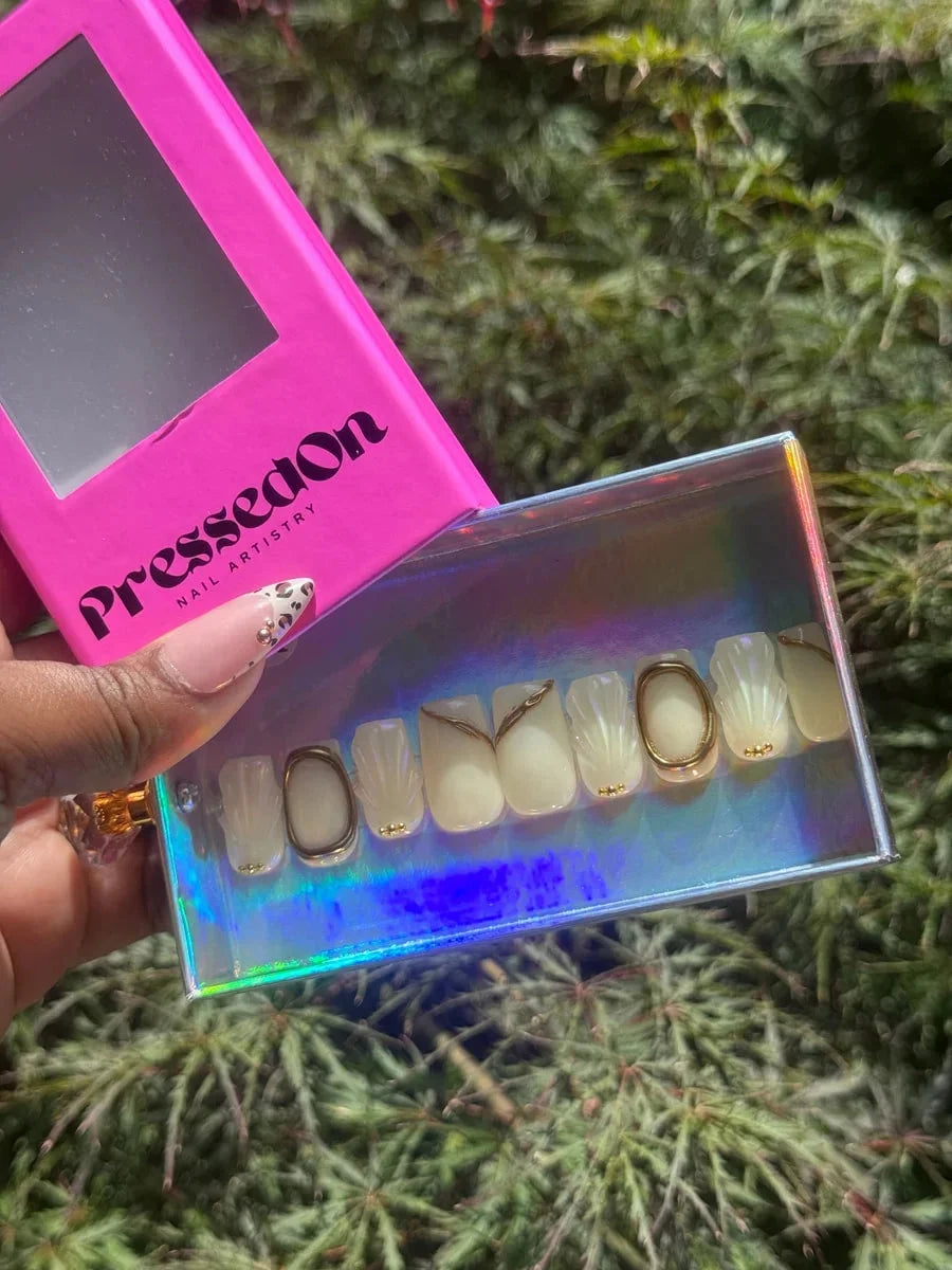 Ivory white super short press-on nails feature 3D seashell designs and gold accents. Some nails include gold rings and embedded detailing.