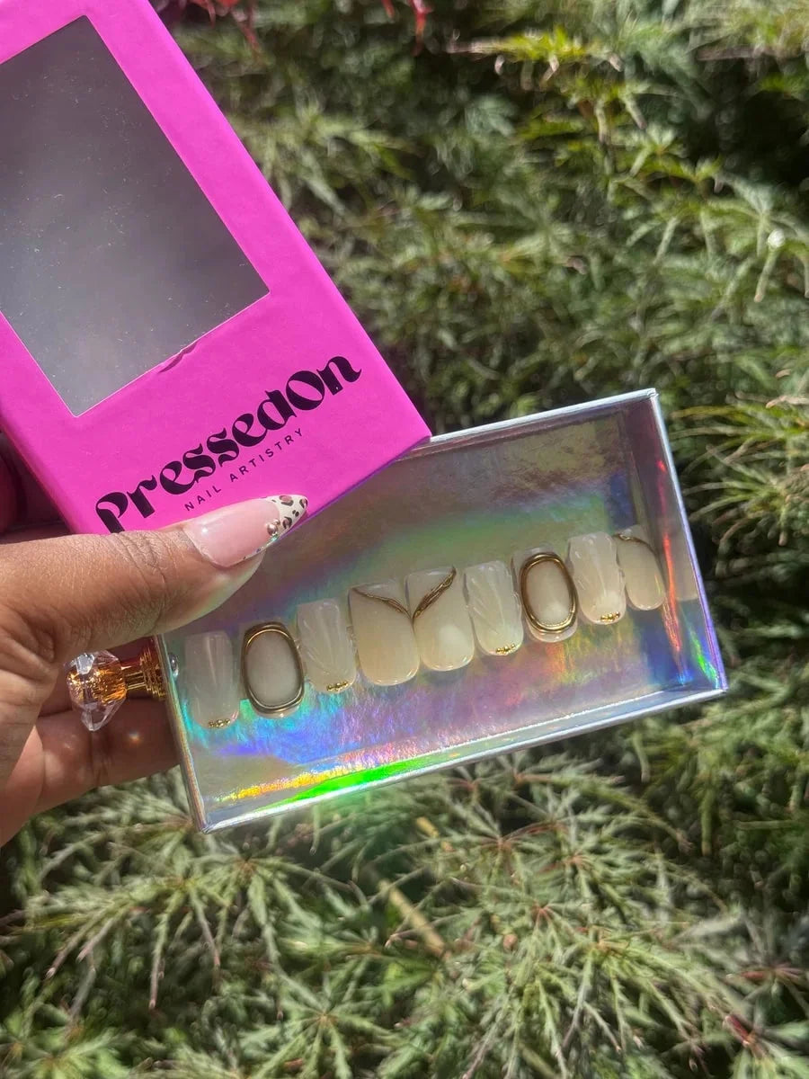 Short ivory press-on nails feature gold accents and 3D designs. Some nails have gold ring and line details.