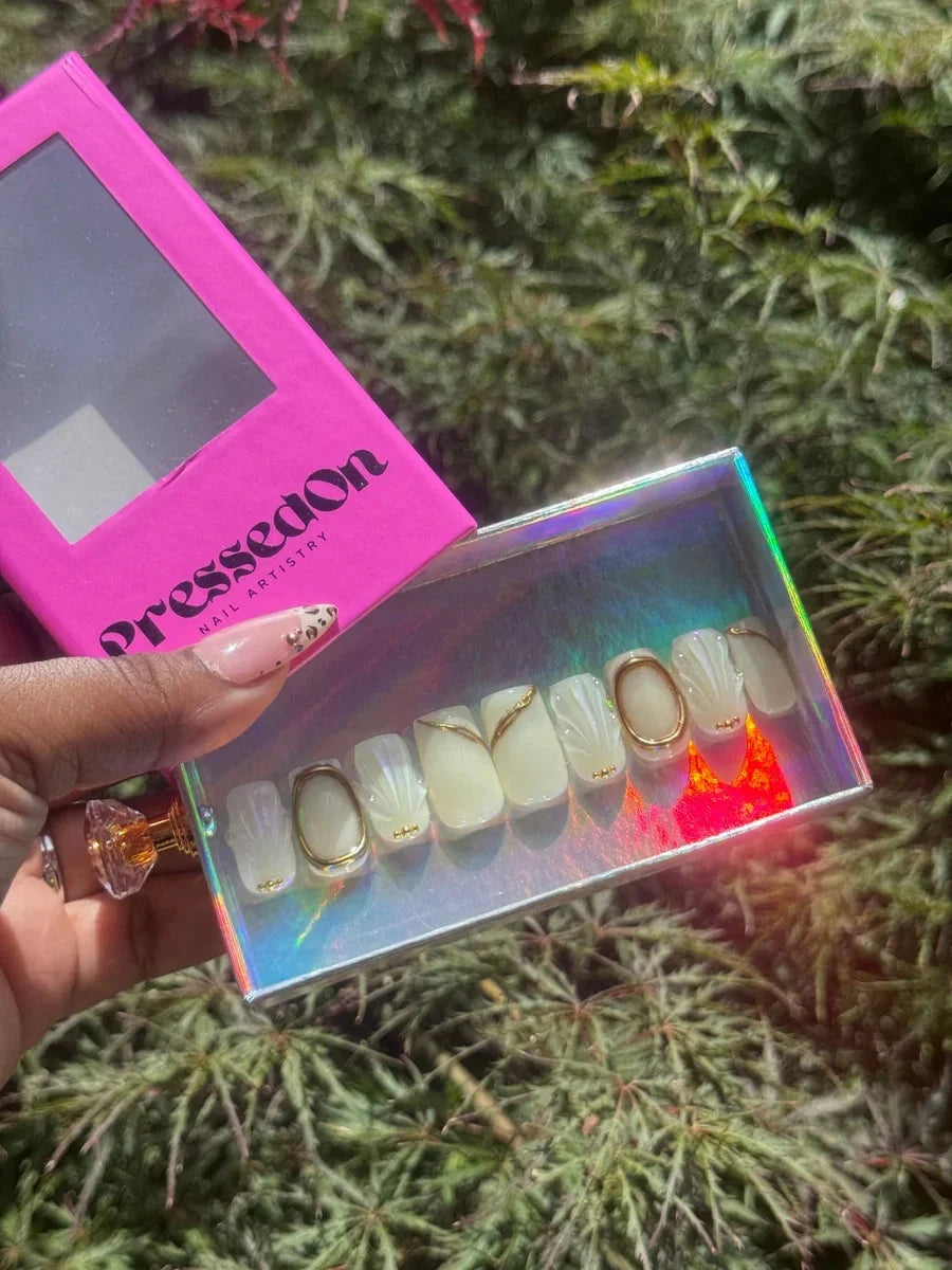 Ivory super short press-on nails feature 3D accents, including a seashell design, with gold details like studs, swirls and ring accents.