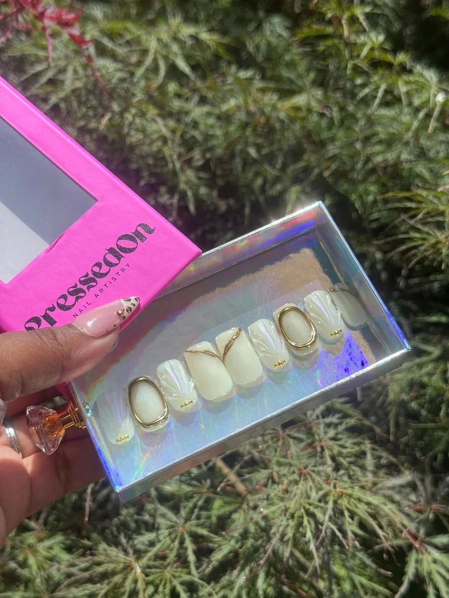 Ivory super short press-on nails feature 3D gold details, including gold rings and seashell-like patterns.