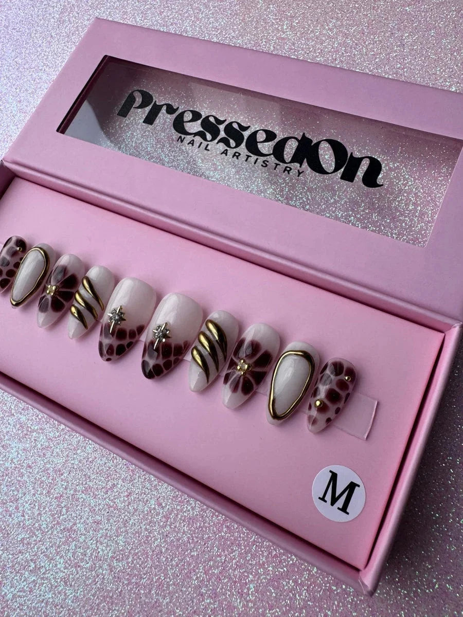 Set of super short press-on nails with bronzed brown, white and gold designs. They feature floral patterns, geometric shapes, spots, a shimmering star embellishment and gold accents.