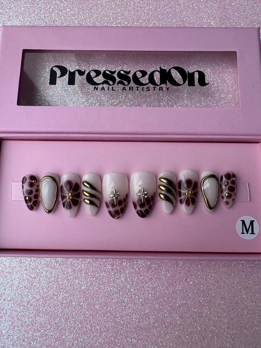 Super short press-on nails featuring a mix of bronzed brown, gold and white designs. Some nails have floral patterns, gold stripes, leopard spots, star embellishments and gold outlines.