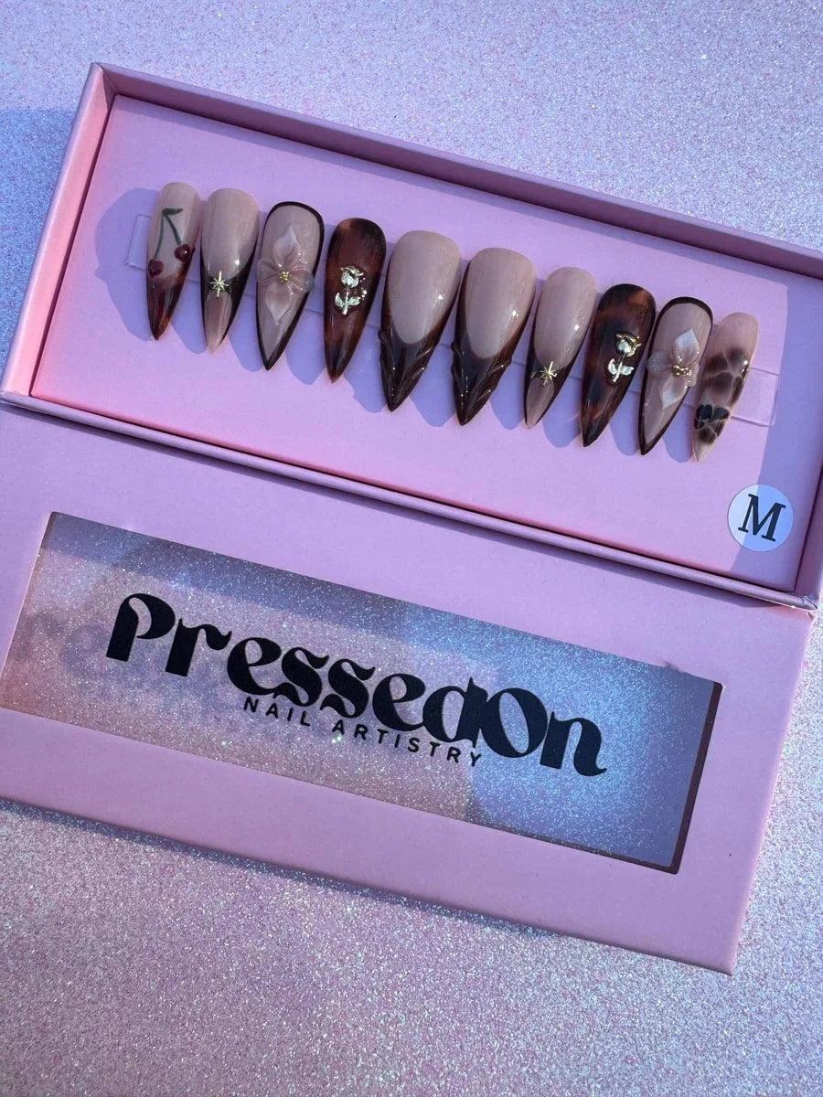 Set of medium brown stiletto press-on nails with cherry, 3D flower and gold rose, gold star accents and brown French tips. Some nails feature a tortoise shell pattern.