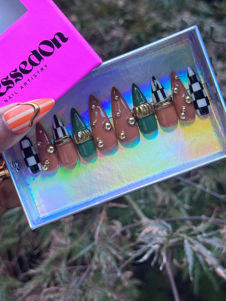 Set of stiletto press-on nails with a black and white checkmate pattern, brown and green, adorned with gold beads and rings.