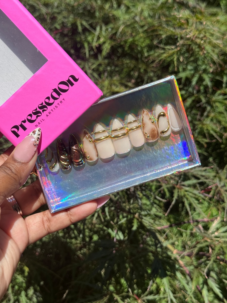 Short press-on nails with a mix of nude, brown and chrome designs, featuring gold rings and stud embellishments. The nail set includes a variety of styles with gold accents.