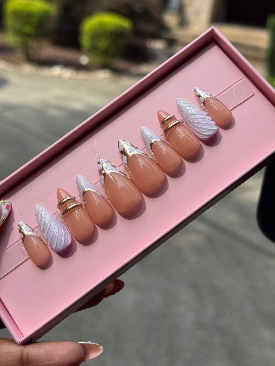 Set of short press-on nails featuring a nude base, cloud-like white and chrome accents, gold rings, and French tips.