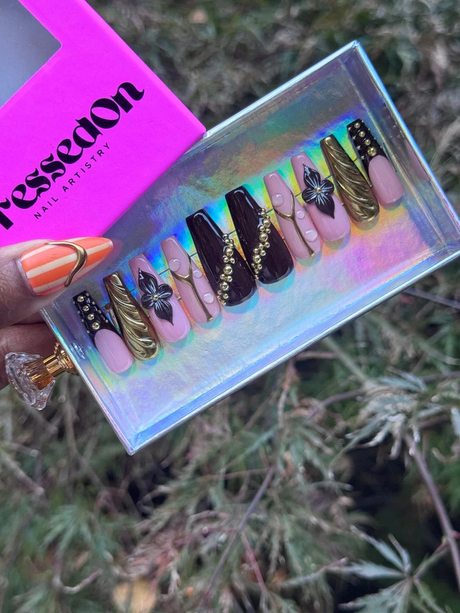 This is a set of medium-length coffin-shaped press-on nails. They feature a cocoa luxe color scheme with gold accents, including beads and flower designs.