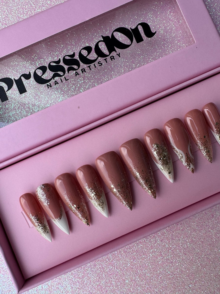 These are medium-length press-on nails with a nude base color and white French tips accented with glitter. The nails have a pointed shape.