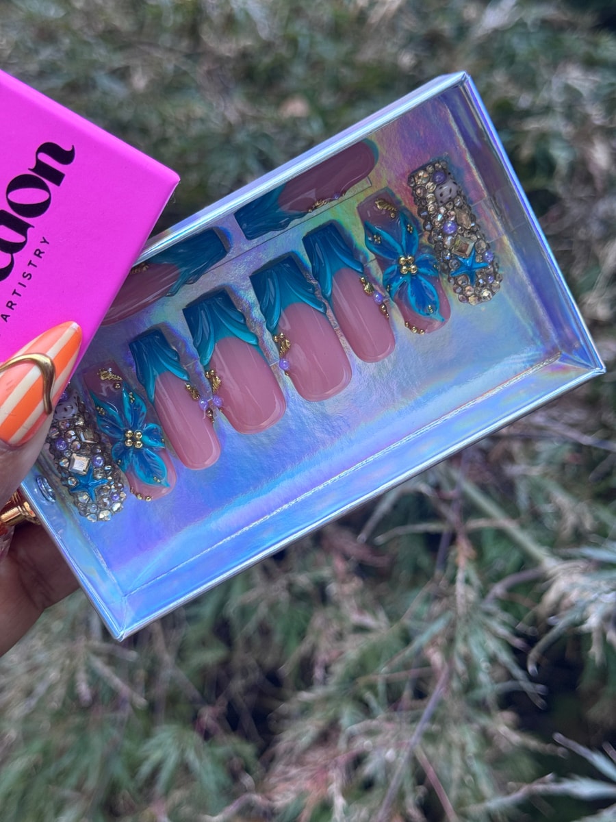 Medium-length press-on nails featuring diamond tide gems, blue floral accents, and gold beads. 