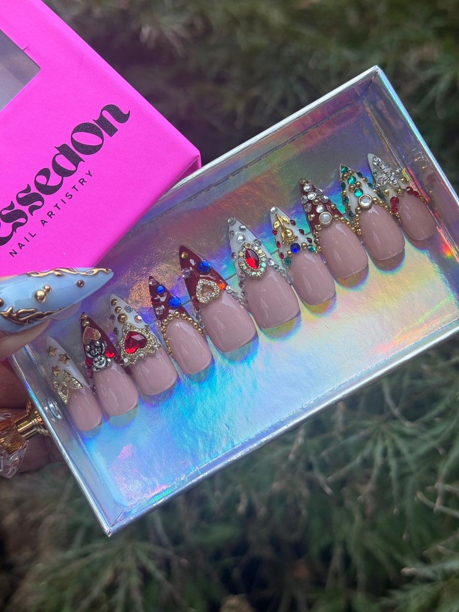 Set of stiletto-shaped short press-on nails with a nude base, adorned with rhinestones, jewels, and golden accents in different ornate designs.